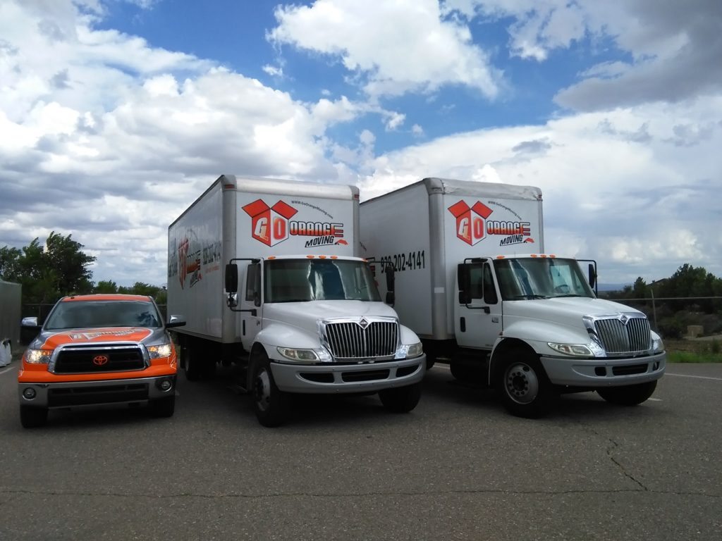 Three trucks parked in a parking lot with cars behind them.
