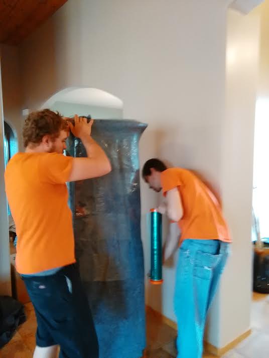 Two men in orange shirts are working on a large object.