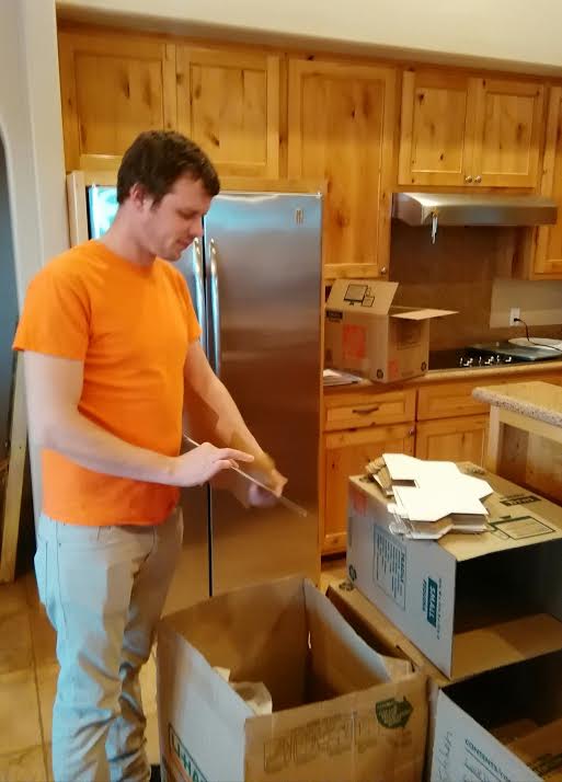 A man in an orange shirt is standing next to boxes.