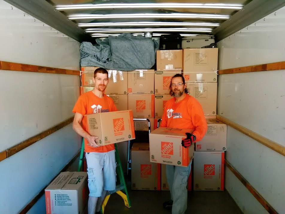Two men in orange shirts holding boxes inside a truck.